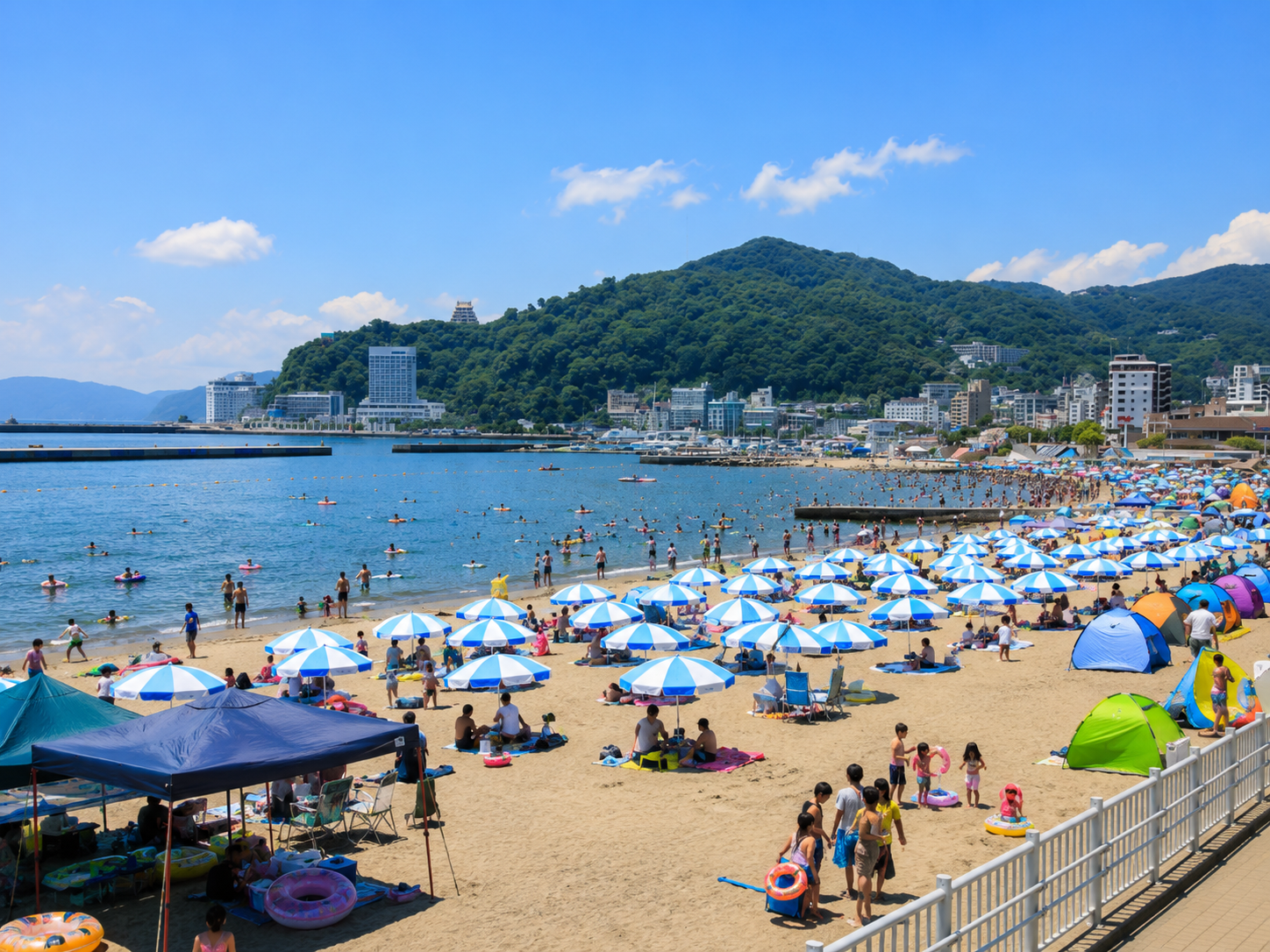 海水浴シーズンで賑わう熱海サンビーチ。青と白のパラソルが並ぶ砂浜